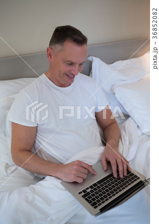 Man using laptop on bed in bedroom 36852082