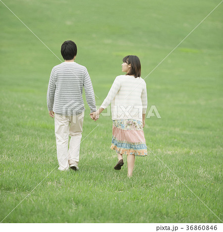 草原で手をつなぐカップルの後姿の写真素材