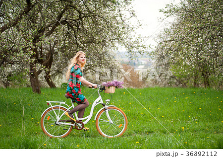 Woman riding vintage white bicycle with flowers basket 36892112