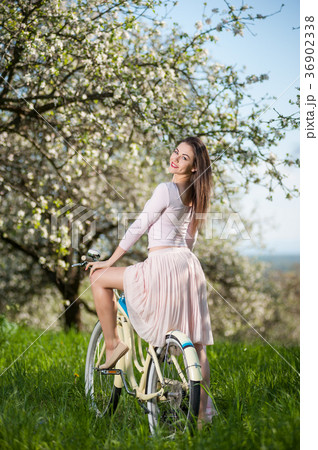 Beautiful female cyclist with retro bicycle in the spring garden Beautiful female cyclist with retro bicycle in the spring garden 36902338