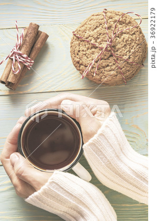 Woman in sweater holds cup of tea on wooden table 36922179