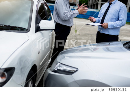 Insurance agent writing on clipboard while examining car after a Insurance agent writing on clipboard while examining car after a 36950151