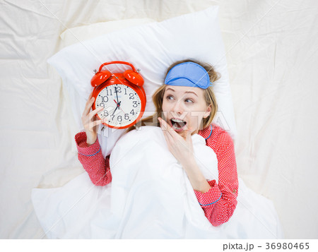 Shocked woman wearing pajamas holding clock overslept Shocked woman wearing pajamas holding clock overslept 36980465