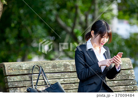 スマホを持ったスーツの女性　OL　ビジネス　スーツ　ポートレート　リクルート　緑背景　 37009484