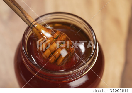 pouring organic honey from dipper into glass jar 37009611