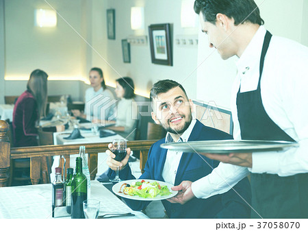 Waiter serving delicious salads to handsome young man at restaurant 37058070