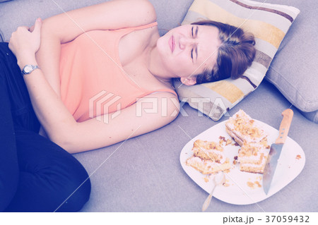 Girl is having a stomach ache after eating many cake Girl is having a stomach ache after eating many cake 37059432