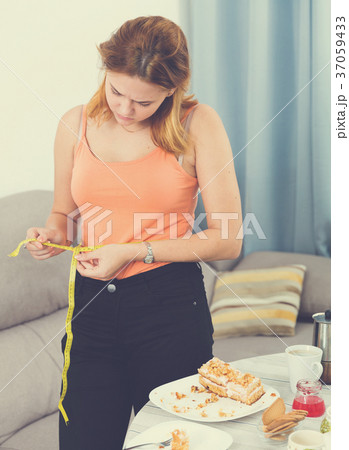 sad female making measurement after eating cake sad female making measurement after eating cake 37059433