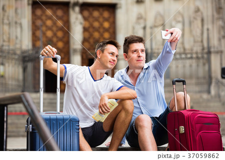 Two guys with luggage taking selfie in city at summer day 37059862