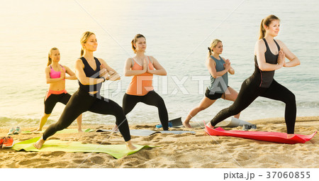 Women practicing yoga position on sandy beach 37060855