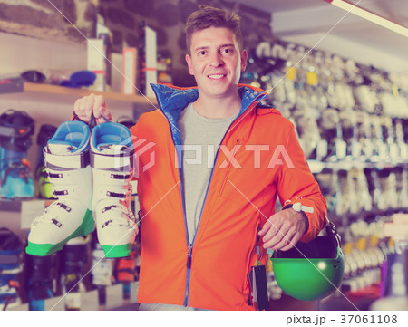 Adult man in jacket and helmet is demonstrating his choice of boots for skiing. 37061108