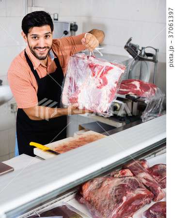 Smilling butcher is offering meat to clients in market. Smilling butcher is offering meat to clients in market. 37061397