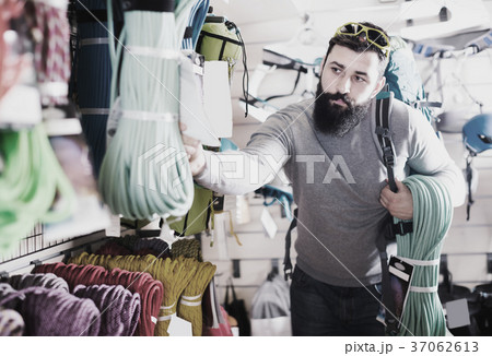 interested male customer examining climbing equipment in sports equipment store 37062613
