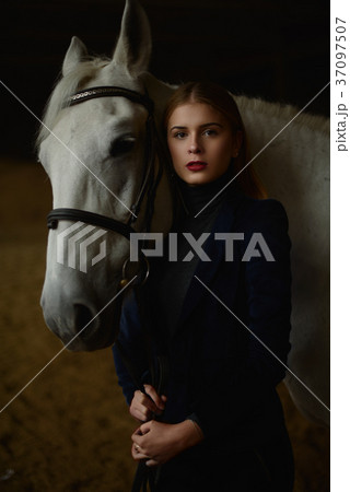 Serious blonde in blue jacket stands with a horse. 37097507