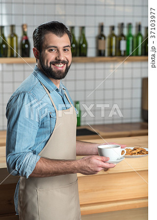 Handsome friendly waiter smiling while holding a Handsome friendly waiter smiling while holding a 37103977