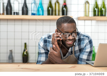 Cheerful young waiter talking on the phone while 37104009
