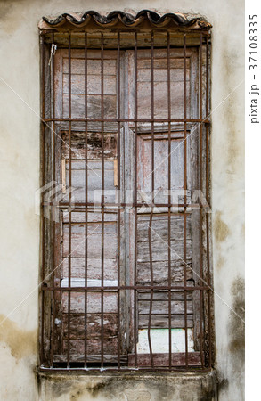 Old unpainted white shutters in window behind rusted iron bars o Old unpainted white shutters in window behind rusted iron bars o 37108335