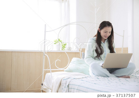 ベッドの上でパソコンを使う女の子の写真素材