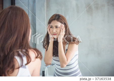 woman unhappy while watching her face in mirror 37163538