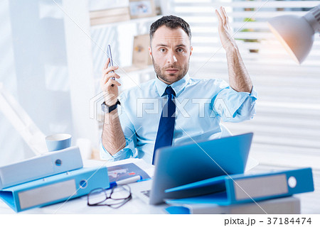 Indignant young worker sitting with a smartphone 37184474