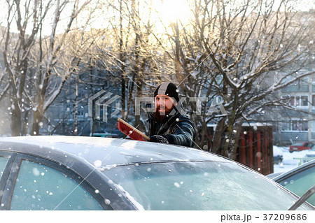 man cleans snow from the glass at car 37209686