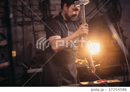 Blacksmith working metal with hammer on anvil in Blacksmith working metal with hammer on anvil in 37254586