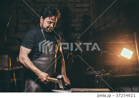 Blacksmith working metal with hammer on anvil in Blacksmith working metal with hammer on anvil in 37254621