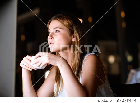 Businesswoman drinking coffee in office at night. Businesswoman drinking coffee in office at night. 37278444