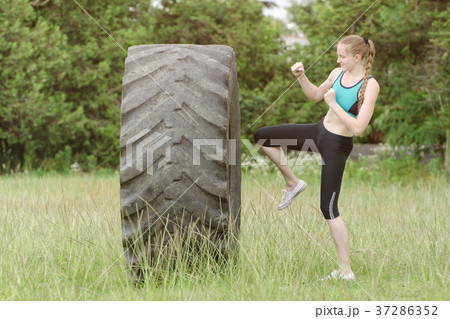 Girl in sports clothes is hitting tire with knee 37286352