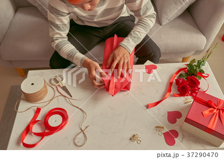 A man wrapping gifts in red ribbon and fresh roses 37290470