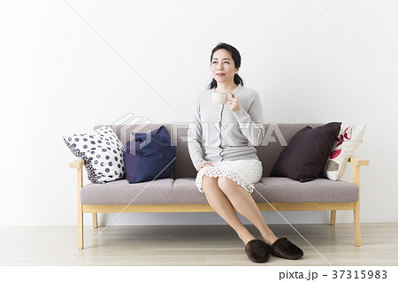 ソファに座ってコーヒーを飲むミドル女性の写真素材