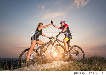 Cyclist couple with mountain bikes on the hill at sunset Cyclist couple with mountain bikes on the hill at sunset 37317334