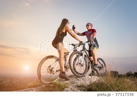 Cyclist couple with mountain bikes on the hill at sunset Cyclist couple with mountain bikes on the hill at sunset 37317336