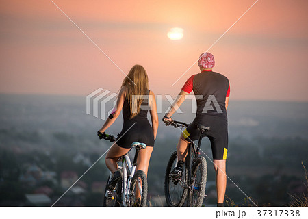 Couple bicyclist with mountain bikes on the hill at sunset 37317338