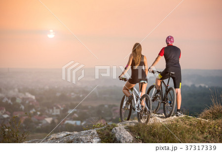 Cyclist couple with mountain bikes on the hill at sunset Cyclist couple with mountain bikes on the hill at sunset 37317339