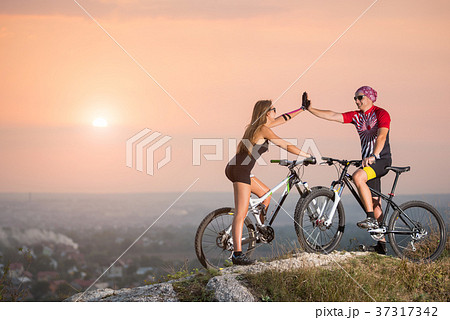 Cyclist couple with mountain bikes on the hill at sunset 37317342