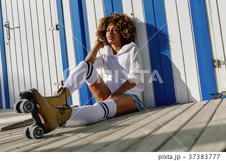 Young black woman on roller skates sitting near a beach hut. 37383777
