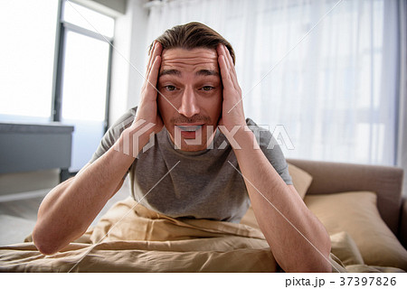 Depressed guy having a migraine in bedroom 37397826