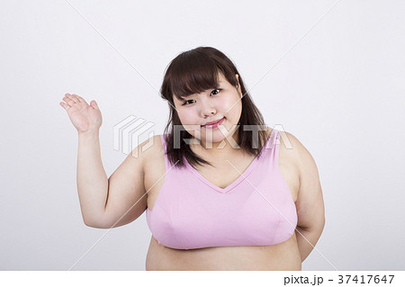 白い背景の前で右手のひら上に向けている笑顔の太った若い女性 37417647