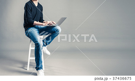 パソコンを持って椅子に座っているカジュアルな服装の男性の写真素材