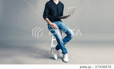 パソコンを持って椅子に座っているカジュアルな服装の男性の写真素材
