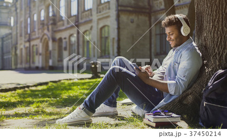 Young male in headphones sitting on grass, leaning Young male in headphones sitting on grass, leaning 37450214