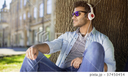 Multiracial guy leaning against tree in headphones 37450454