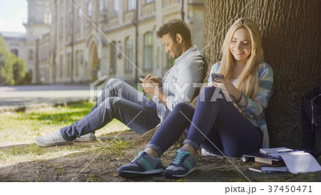 Young people sitting under tree, using cellphone Young people sitting under tree, using cellphone 37450471