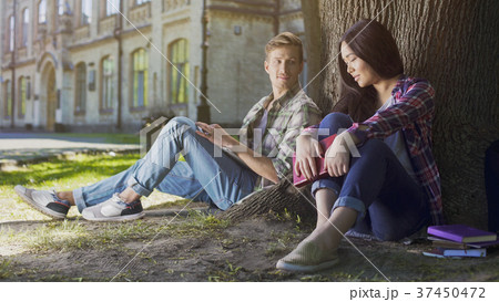 Two young people sitting under tree, girl looking Two young people sitting under tree, girl looking 37450472