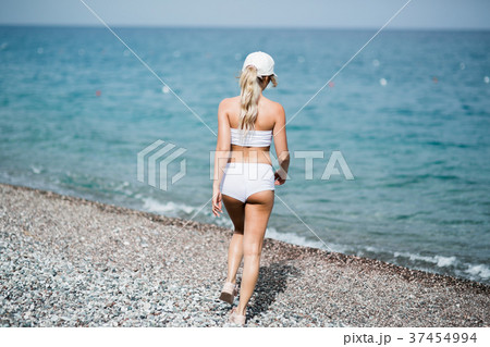 Back view of fitness girl walking along the beach 37454994