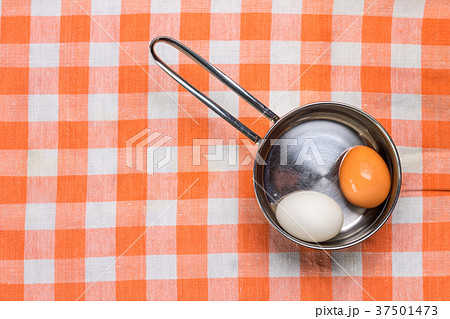 Two eggs in saucepan on checered towel 37501473