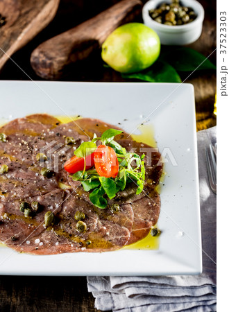 Beef carpaccio on white plate, wooden background Beef carpaccio on white plate, wooden background 37523303