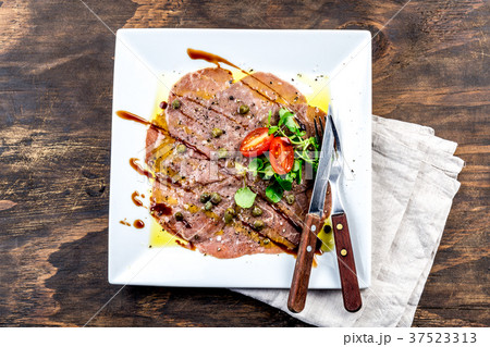 Raw BEEF CARPACCIO on white plate, wooden 37523313