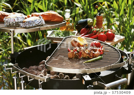 Barbecuing out of doors (kebabs, vegetables, potatoes, baguette) 37530409
